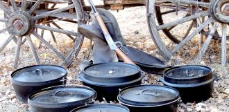 Dutch ovens in front of old time rifle, horse saddle, and wagon